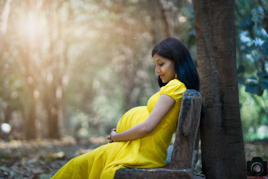 Rajani sitting on a bench in a garden in her Maternity Photoshoot in Yellow Gown|Photographer in Pune,India